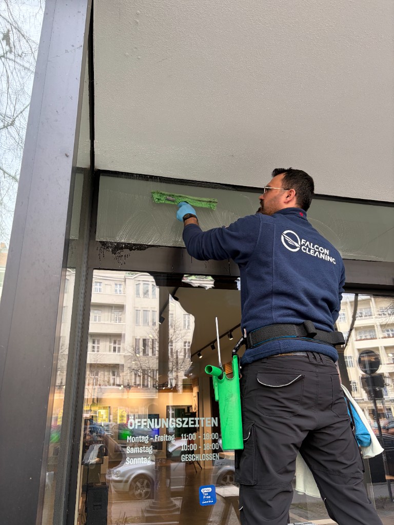 Falcon Cleaning Mitarbeiter bei der Fensterreinigung: Reinigung einer Glasfront an einem Geschäftseingang
