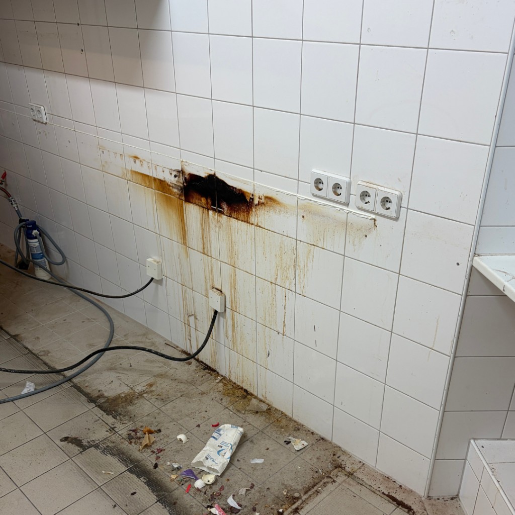 Gewerbeküche vor der Reinigung: Fett- und Schmutzrückstände an Wand und Boden