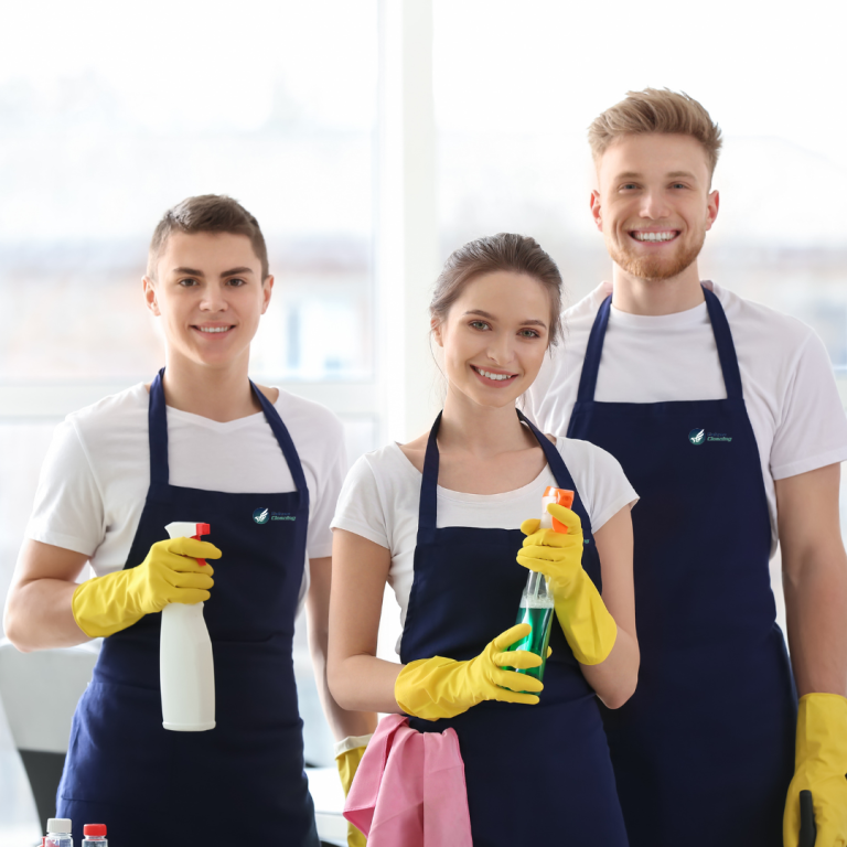 Drei fröhliche Reinigungskräfte von Falcon Cleaning, in blauen Schürzen mit Putzmitteln in der Hand.